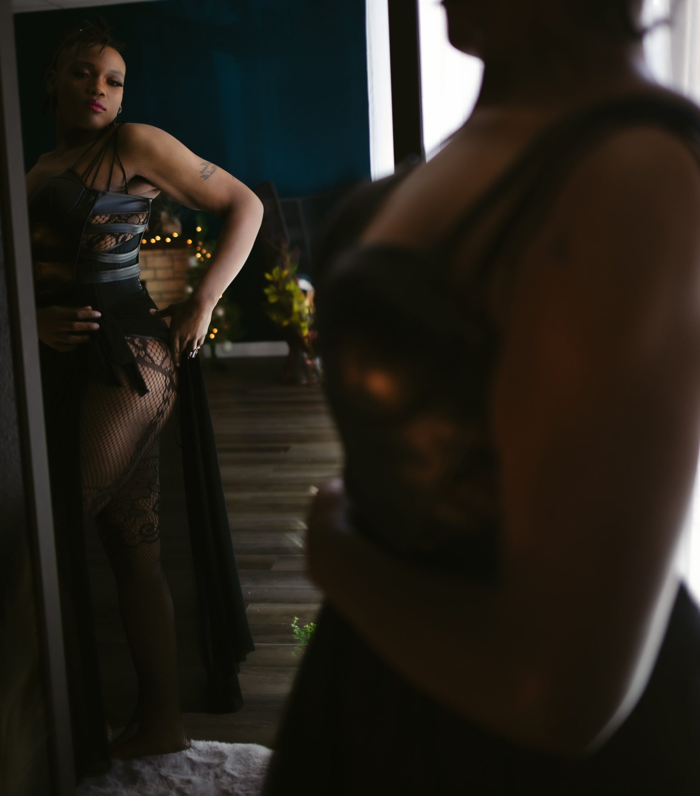A woman poses in front of a mirror wearing a black dress and lace stockings during a Las Vegas boudoir photography session