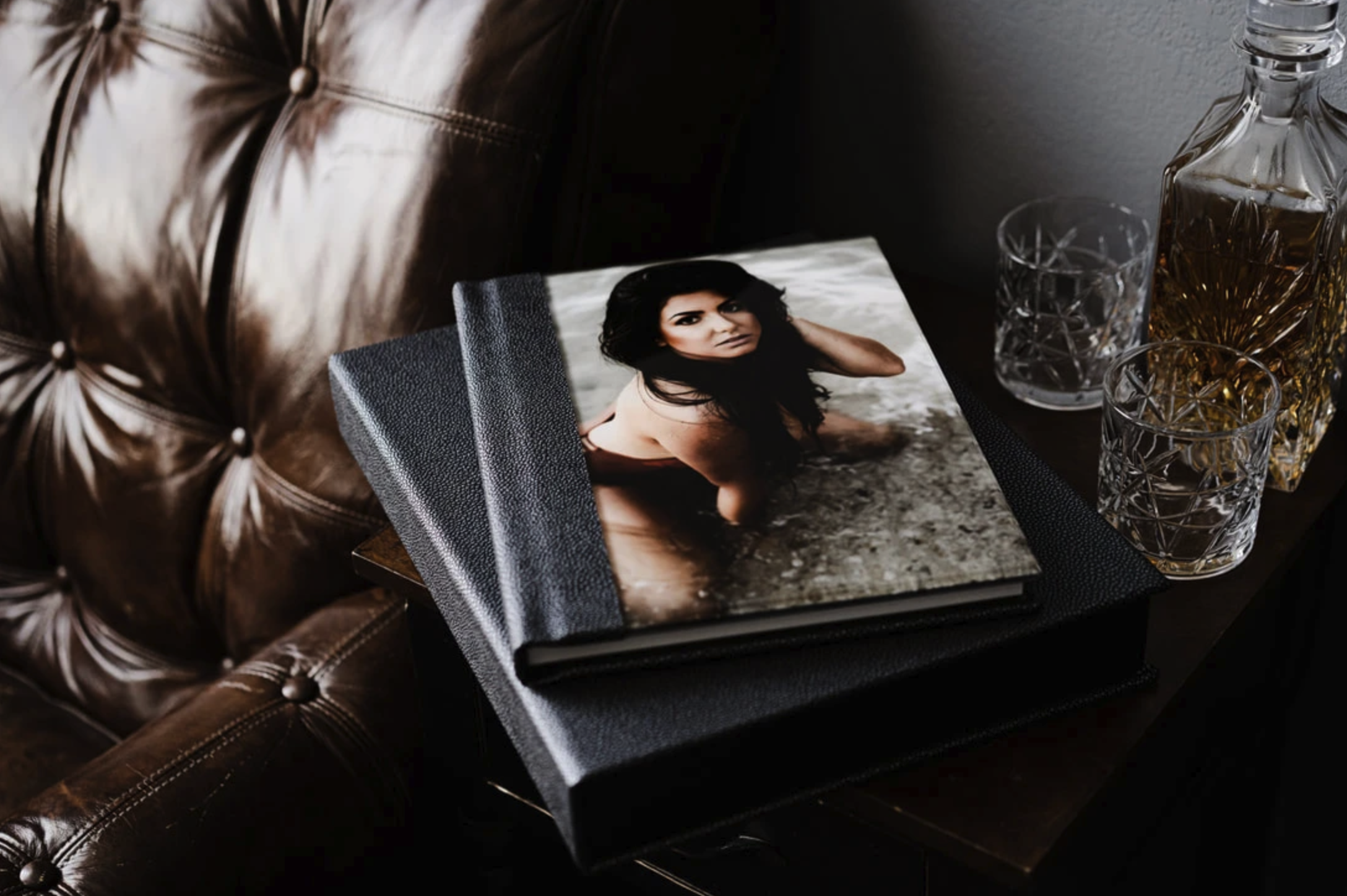 Luxury boudoir photo album stacked next to whiskey glasses and decanter on leather chair