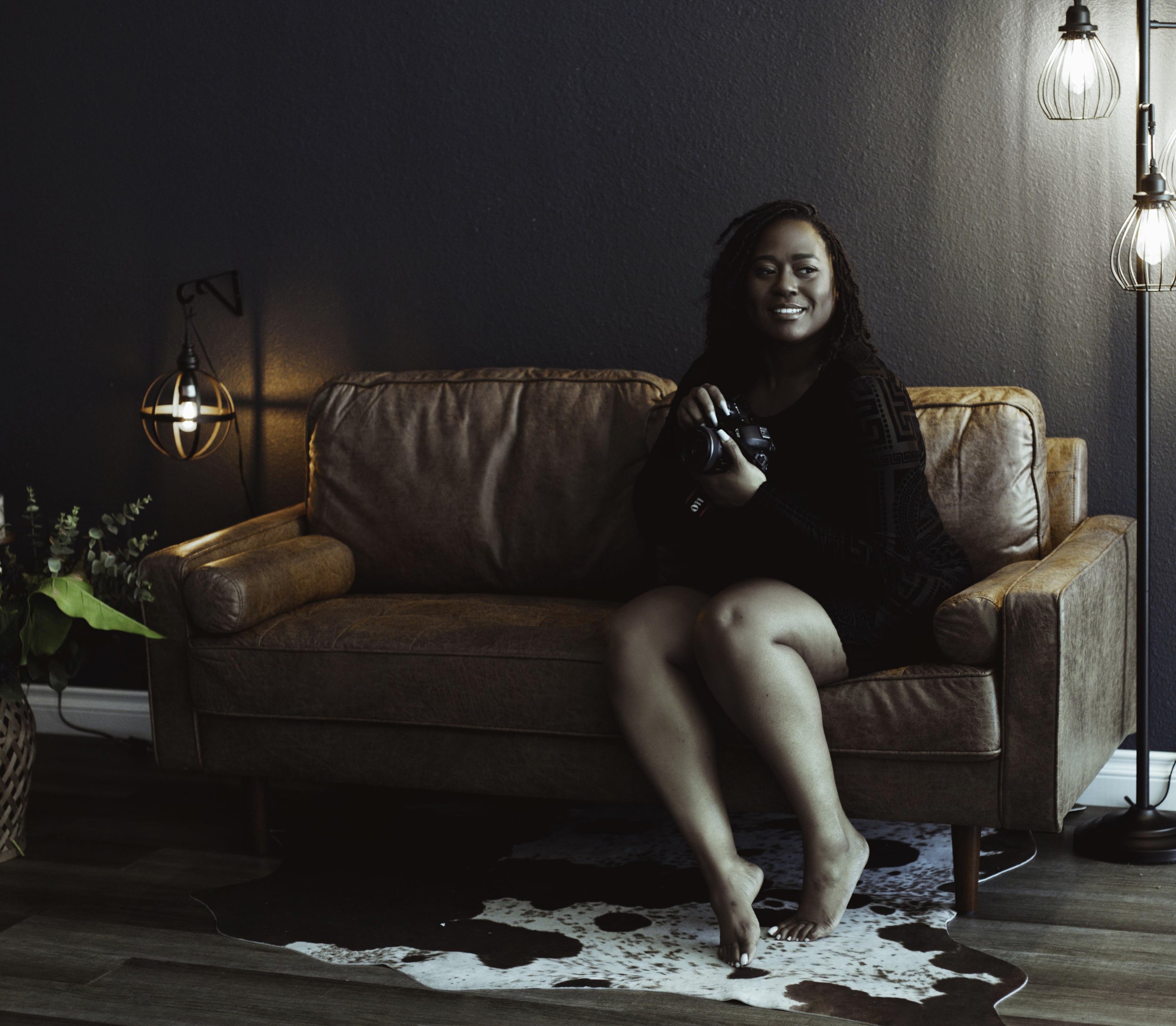 Las Vegas boudoir photographer Latasha Nicole of Latasha Nicole Boudoir sitting on a leather sofa in a dark moody studio holding a camera