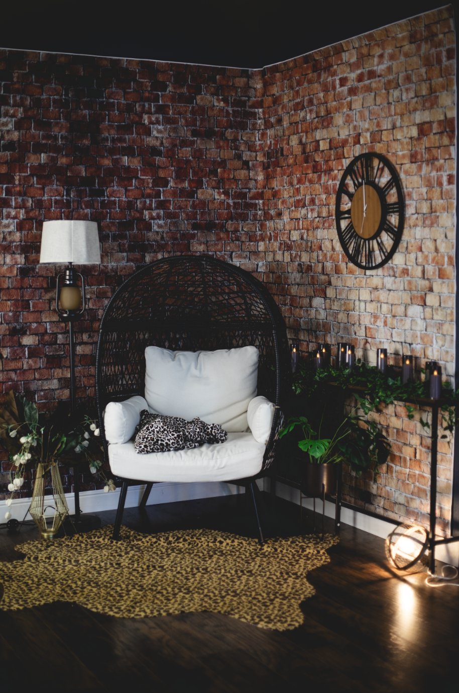 A black egg-crate chair with white cusions sits in from of a brick wall backdrop with a leopard print rug in the front.