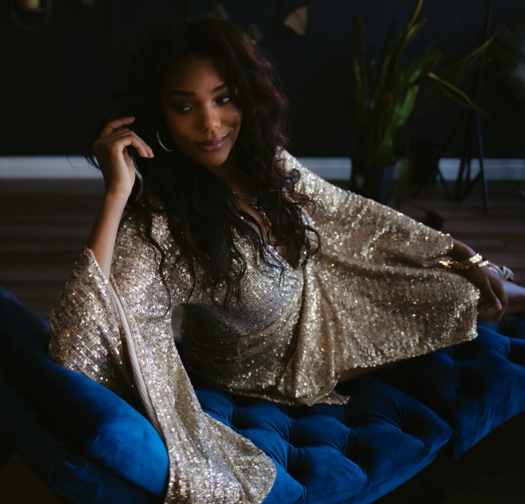A beautiful woman reclines on a blue velvet lounger wearing a gold sparkly dress during a Vegas boudoir session.