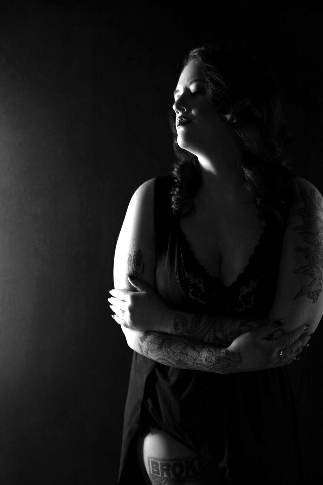 Black and white boudoir photograph of a woman with arms wrapped around herself, eyes closed, fully present
